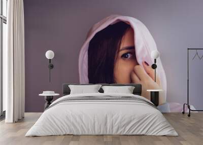 The woman hides her face behind the hood. Stylish female posing in a hoodie. Portrait of a young woman covering her face with a hood Wall mural