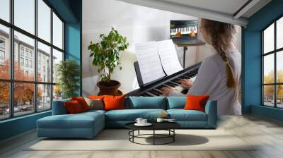 Girl learning to play the piano in distance learning via laptop over the Internet Wall mural