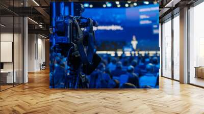 Back view of a professional video camera recording a speaker at a crowded business conference with audience. Wall mural