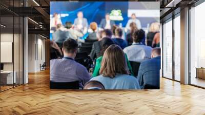 Focused audience members view a panel discussion at a conference. The image captures engagement and diverse professionals in a blurred background. Wall mural