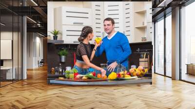 Young couple having fun in the kitchen preparing dinner Wall mural