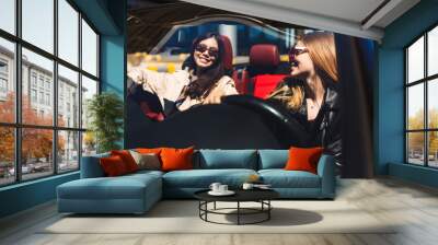 Joyful girls in sunglasses happily spending time together driving cabriolet on city streets outdoor Wall mural