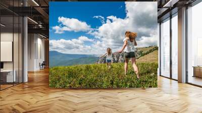 Two girls running on the meadow with mountains and cloudscape on background. Wall mural