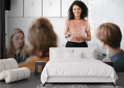 Portrait of beautiful African American lady with dark curly hair standing near board and giving presentation to colleagues in office. Young cheerful business woman speaking with her coworkers Wall mural