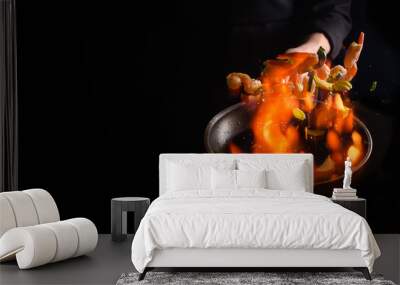 Seafood and their preparation, a professional chef cooks shrimps with vegetables with fire. On a black background, a banner, cooking and recipes. Restaurant and hotel service concept. Wall mural