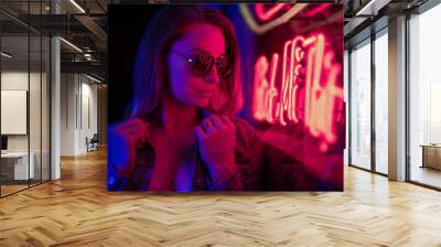 Sexy portrait of a young girl in sunglasses and with in the night city, with creative light on the background of neon lamps. Night clubs, parties, strip business, night life. Wall mural