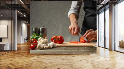 The concept of nutrition. The chef cuts tomatoes on the background of a concrete wall, with ingredients for cooking pizza, pizza sauce, sauce for Italian pasta Wall mural