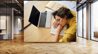 Top view of young tired woman dreamy asleep on desk with laptop and documents under head at workplace Wall mural