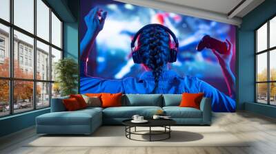 Young girl in headphones plays a video game on the TV in the evening. Gamer with a joystick. Online gaming with friends, competitions, win. Fun entertainment. Teens play puzzle games. Back view Wall mural