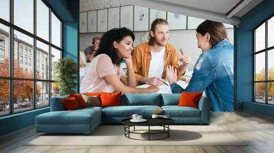 Young man and two girls working together in office. Group of students studying together in classroom. Group of cool young people happily talking and discussion something together Wall mural