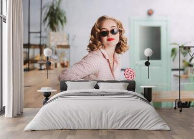 Young pretty lady in sunglasses sitting at the bar counter with lollipop candy while spending time in cafe Wall mural