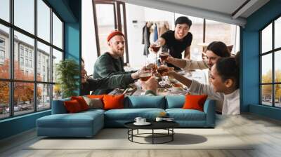 Young smiling asian man in eyeglasses and black T-shirt cheers glasses of wine with colleagues. Group of attractive international friends spending time together on lunch in cozy cafe Wall mural