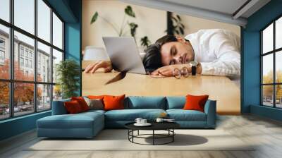 Young tired man with laptop sleeping on desk at work in office Wall mural