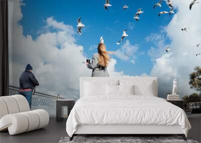 Young woman feeds seagulls. Сoastline scene with girl. Concept of travel Wall mural