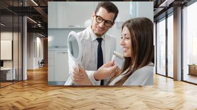 Young man dentist in white coat show veneers enamel color palette for beautiful patient woman Wall mural