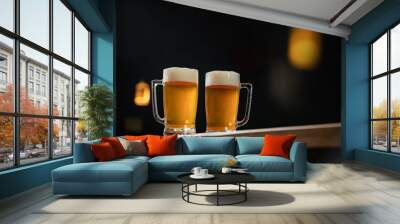 two cold mugs with beer, with overflowing foam, on wooden table and dark background, space for writing Wall mural