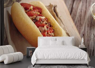 Hot dog with onion, ketchup and mustard on a white chopping board on a wooden table. Ketchup and mustard in two transparent bowls. Wall mural