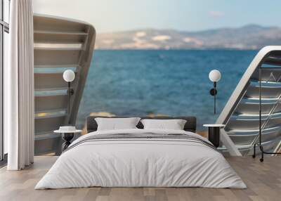 View of two white foldable benches near the sea, concept of vacation and summer. Bright blue water in the background Wall mural