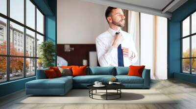 Businessman fixing his tie in a hotel room Wall mural