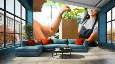 Closeup of a worker presenting a potted plant in an eco-friendly paper bag to a customer at a plant boutique Wall mural