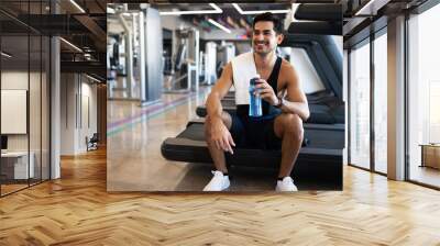 Happy young hispanic man sitting on a treadmill Wall mural