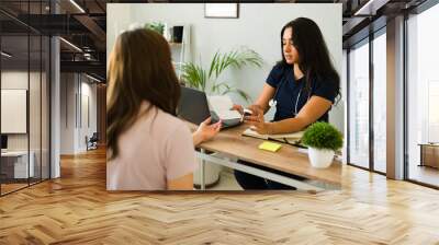 Hispanic female doctor discussing treatment with patient while holding prescription and medication bottle in her office Wall mural