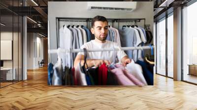 Male stylist choosing stylish garments in a trendy fashion store filled with customers looking for the latest menswear trends Wall mural