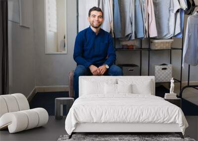 Portrait of a Hispanic man sitting in his modern walk in closet with clothes rack and storage boxes Wall mural