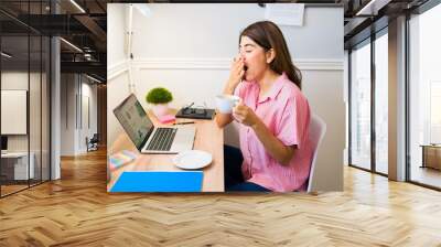 Tired and sleepy woman drinking coffee to start her remote work Wall mural