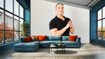 Young man clapping and smiling happily against a white background, radiating positive energy and celebrating success Wall mural