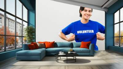 Young woman beaming with pride as she points to her volunteer t-shirt, representing the spirit of kindness and generosity in charity work and activism Wall mural