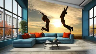 Couple or friends jumping on the beach at sunset Wall mural