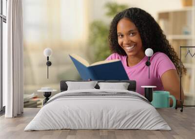 Happy black reader looking at camera holding book Wall mural