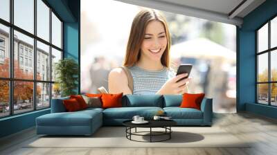 Happy girl walking in the street checking phone Wall mural