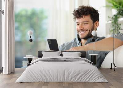 Happy man using cell phone on a couch at home Wall mural