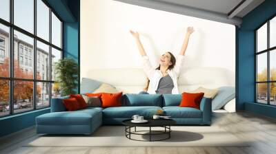 Happy woman raising arms and looking above on a couch Wall mural