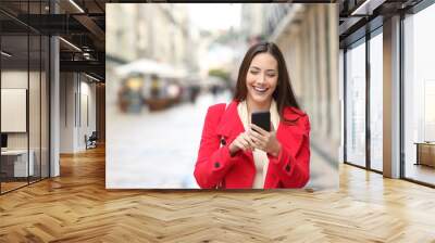 Happy woman walking using smart phone in the street Wall mural