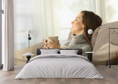 Pensive woman relaxing at home in winter Wall mural