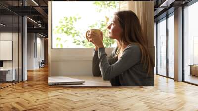 Relaxed woman looking through a window at home Wall mural