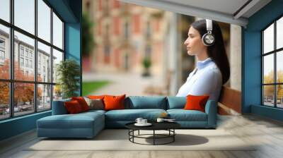 Serious woman sitting in a bench listening to music Wall mural