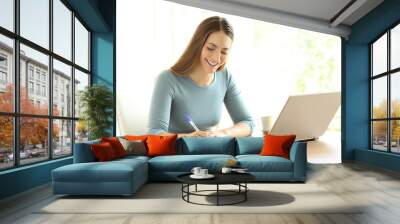 Woman writing notes beside a laptop at home Wall mural