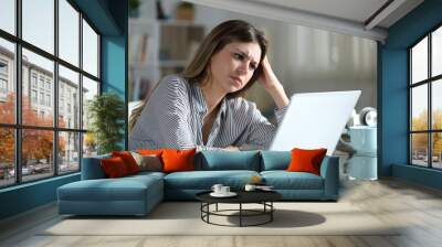 Worried woman is checking laptop content at home Wall mural