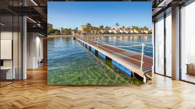 Iron bridge and wooden walkway over the crystalline beach of El Mar de Cristal, in the Mar Menor, Cartagena, Spain with the town in the background Wall mural