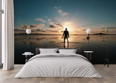 Silhouette of a man standing with his back facing at sunset over the shallow waters of the Mar Menor, Region of Murcia, Spain, creating ripples on the surface of the water Wall mural