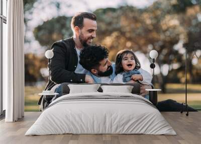 Gay couple enjoying in the park with their little daughter. Proud homosexual family concept. Wall mural