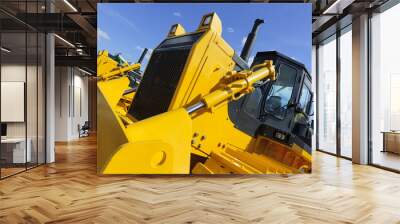 Bulldozer, row of huge yellow powerful construction machines with big scoop and tracks, heavy industry, bottom view, blue sky and white clouds on background  Wall mural