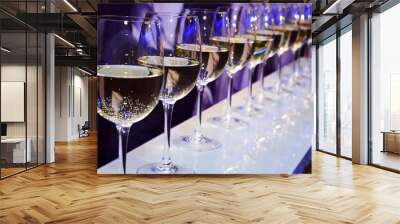 Nightclub wine glasses with white wine lit by party festive lights on dark-purple background, nightlife entertainment industry  Wall mural