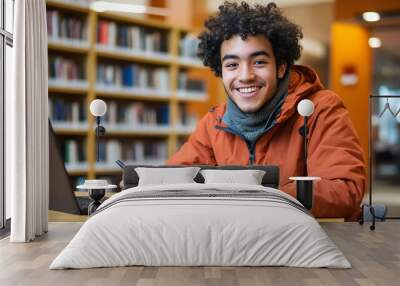 Cheerful man studying in a library with books, laptop, and notebook, bright setting, learning focus Wall mural