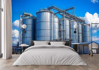 Modern industrial facility with shiny metallic silos under a bright blue sky, showcasing agriculture grain storage Wall mural