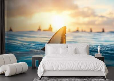 Ocean scene with a dramatic sunset, calm water surface, and a shark fin emerging in the foreground, teeming with distant surfers Wall mural